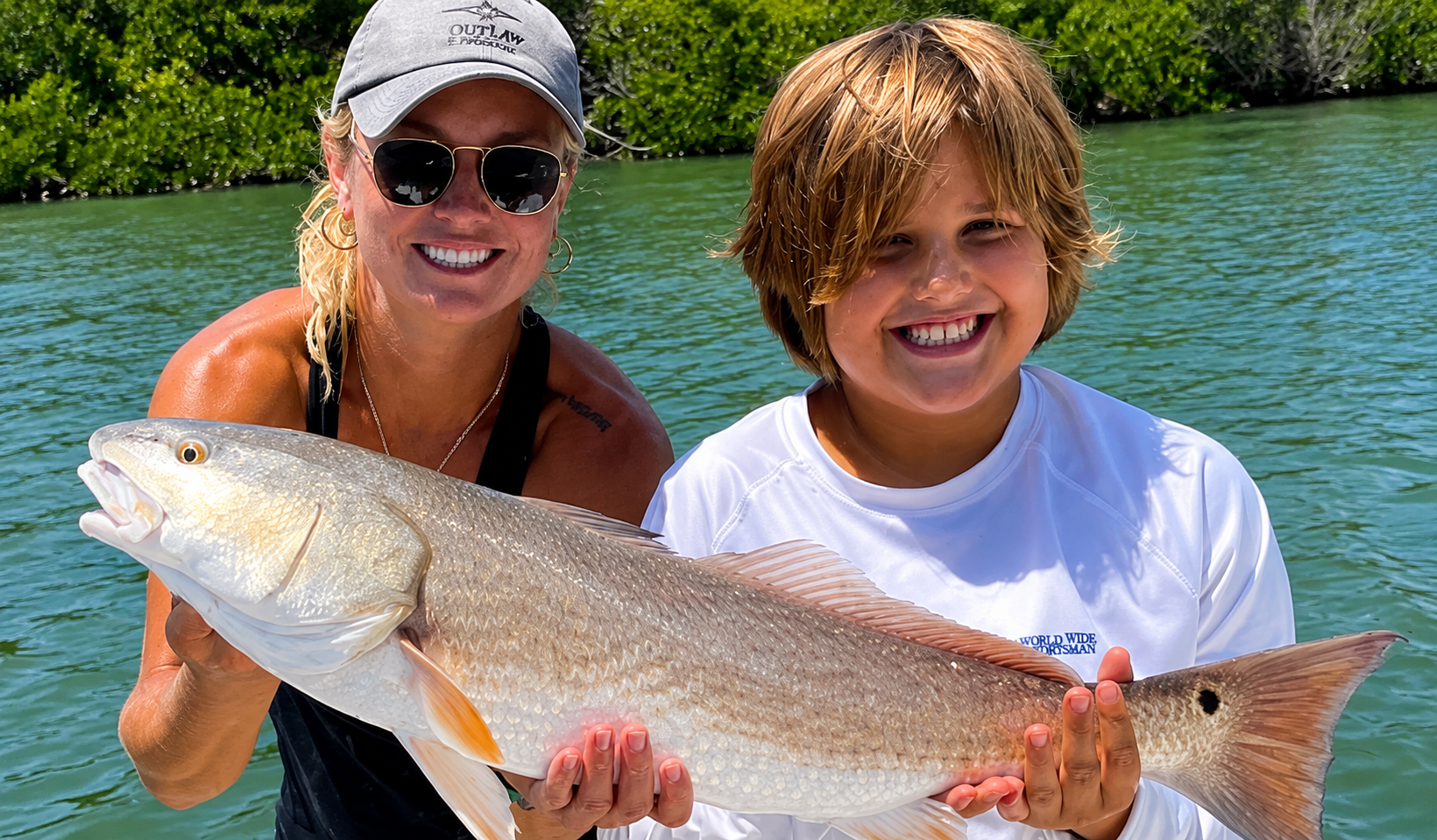 A redfish held up by the captain and a young angler